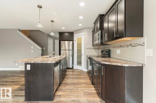 Kitchen featuring dark wood-finish cabinetry, stainless steel appliances, speckled countertops, a tiled backsplash, and recessed lighting - 79 Catalina Crest, Fort Saskatchewan, AB - Indoor Photo Showing Kitchen With Upgraded Kitchen