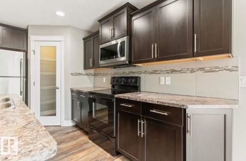 Dark wood-finish cabinetry, stainless steel microwave, black electric range, light-toned countertops, and wood-finish flooring - 79 Catalina Crest, Fort Saskatchewan, AB - Indoor Photo Showing Kitchen