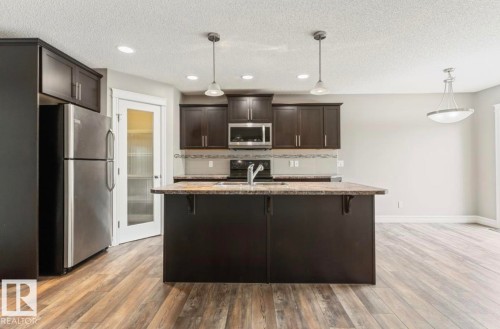 Kitchen featuring dark wood cabinetry, a central island with a sink, stainless steel appliances, and wood-finish flooring - 79 Catalina Crest, Fort Saskatchewan, AB - Indoor Photo Showing Kitchen With Upgraded Kitchen