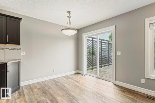 Wood-finish flooring, dark cabinetry with a light countertop, pendant light fixture, and sliding glass door - 79 Catalina Crest, Fort Saskatchewan, AB - Indoor Photo Showing Other Room