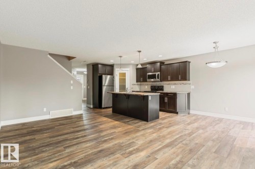 Wood-finish flooring throughout, kitchen with dark wood cabinetry, stainless steel appliances, central island, and pendant lighting - 79 Catalina Crest, Fort Saskatchewan, AB - Indoor Photo Showing Kitchen With Upgraded Kitchen