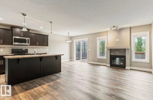 Kitchen with dark wood cabinetry, a central island, and stainless steel appliances - 79 Catalina Crest, Fort Saskatchewan, AB - Indoor Photo Showing Other Room With Fireplace