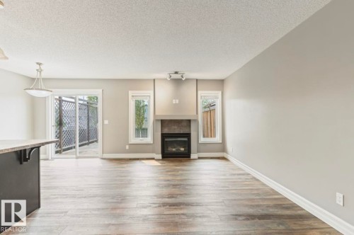 Wood-finish flooring, built-in fireplace with tile surround, white trim, sliding glass door, and a modern pendant light fixture - 79 Catalina Crest, Fort Saskatchewan, AB - Indoor Photo Showing Living Room With Fireplace