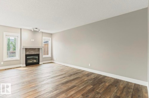 Spacious living area featuring wood-finish flooring, a built-in fireplace with a stone surround, and track lighting - 79 Catalina Crest, Fort Saskatchewan, AB - Indoor Photo Showing Living Room With Fireplace