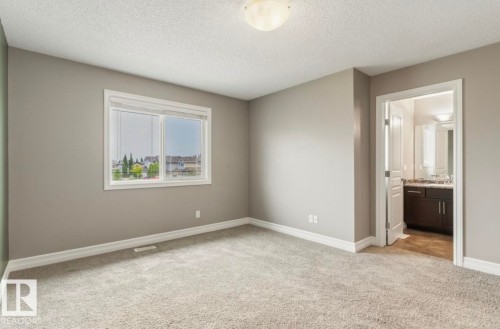Neutral-toned carpeting, ample natural light from a large window, a built-in flush mount ceiling light, and an adjoining bathroom featuring a dark wood-finish vanity with a light-colored countertop - 79 Catalina Crest, Fort Saskatchewan, AB - Indoor Photo Showing Other Room