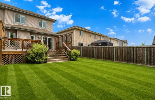 Expansive lawn with striped mowing pattern, leading to a multi-level wood deck and sliding glass door - 79 Catalina Crest, Fort Saskatchewan, AB - Outdoor With Deck Patio Veranda