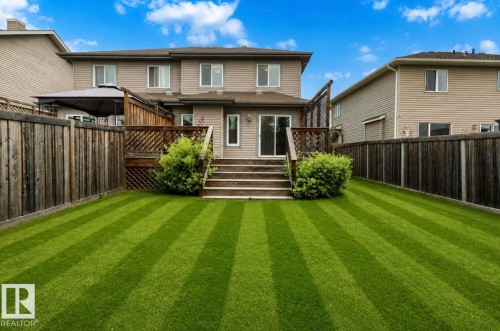 Expansive backyard featuring a manicured lawn, full privacy fencing, a wood deck with steps, and a sliding glass door entry to the home - 79 Catalina Crest, Fort Saskatchewan, AB - Outdoor