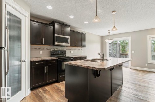 Kitchen featuring dark wood cabinetry, stainless steel appliances, an island with an undermount sink, and wood-finish flooring - 79 Catalina Crest, Fort Saskatchewan, AB - Indoor Photo Showing Kitchen With Double Sink With Upgraded Kitchen