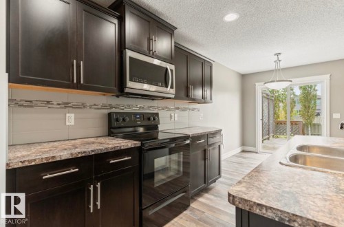 Modern kitchen featuring dark wood-finish cabinetry, stainless steel appliances, a tile backsplash, and wood-finish flooring - 79 Catalina Crest, Fort Saskatchewan, AB - Indoor Photo Showing Kitchen With Double Sink