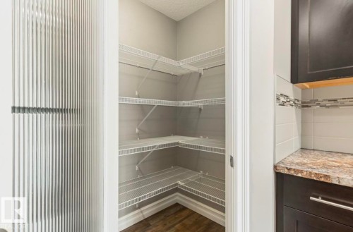 Corner pantry with wire shelving, wood-finish flooring, and a corrugated glass door - 79 Catalina Crest, Fort Saskatchewan, AB - Indoor With Storage