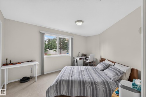 Bright bedroom featuring neutral wall finishes, wood-finish flooring, and a sliding glass door with functional curtain panels opening to natural light - #105 10421 42 Av Nw, Edmonton, AB - Indoor Photo Showing Bedroom