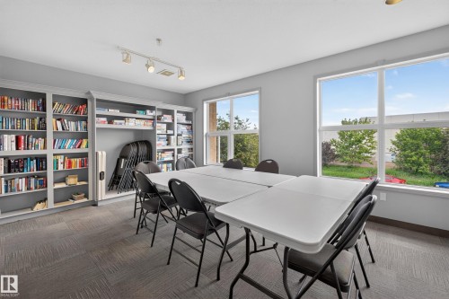 Spacious room featuring multiple large windows, track lighting, extensive built-in shelving, and carpet tile flooring - #105 10421 42 Av Nw, Edmonton, AB - Indoor Photo Showing Dining Room