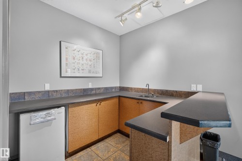 Built-in wet bar featuring a stainless steel sink, dark countertops, and wood-finish cabinetry - #105 10421 42 Av Nw, Edmonton, AB - Indoor
