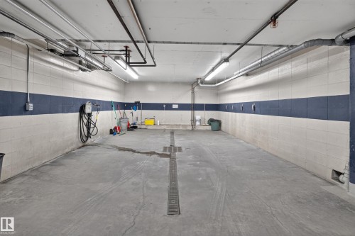 Spacious garage area featuring concrete block walls with a contrasting blue stripe - #105 10421 42 Av Nw, Edmonton, AB - Indoor Photo Showing Garage