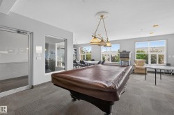 Spacious common area featuring a covered billiards table, fireplace, numerous windows, and grey-toned carpet tile flooring - 
