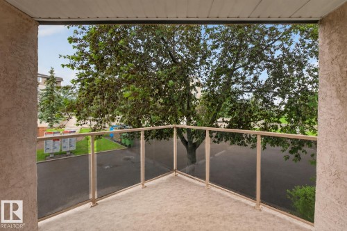 Outdoor balcony featuring a glass panel railing, stucco walls, and a textured concrete floor - #105 10421 42 Av Nw, Edmonton, AB - Outdoor With Balcony