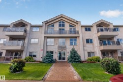Multi-story residential building featuring balconies with glass railings, an arched central entrance, and a paved walkway - 