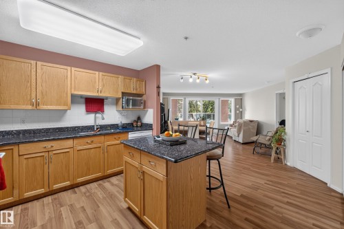 Kitchen featuring wood cabinetry, dark countertops, white subway tile backsplash, and a central island with bar seating - #105 10421 42 Av Nw, Edmonton, AB - Indoor Photo Showing Kitchen