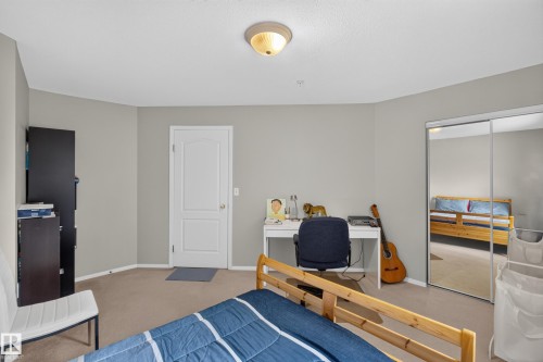 Bedroom featuring neutral paint, carpeted flooring, a ceiling-mounted light fixture, a white paneled door, and mirrored closet doors - #105 10421 42 Av Nw, Edmonton, AB - Indoor Photo Showing Bedroom