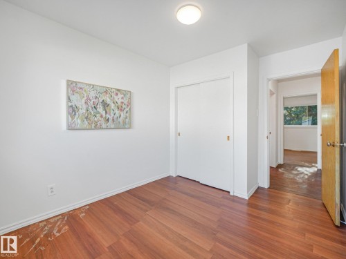Wood-finish flooring with white baseboards, sliding closet doors, and flush-mount ceiling lighting - 6112 105A Street Nw, Edmonton, AB - Indoor Photo Showing Other Room