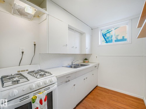 Compact kitchen featuring wood-finish flooring, white cabinetry, a double basin sink, and a white gas range - 6112 105A Street Nw, Edmonton, AB - Indoor Photo Showing Kitchen With Double Sink
