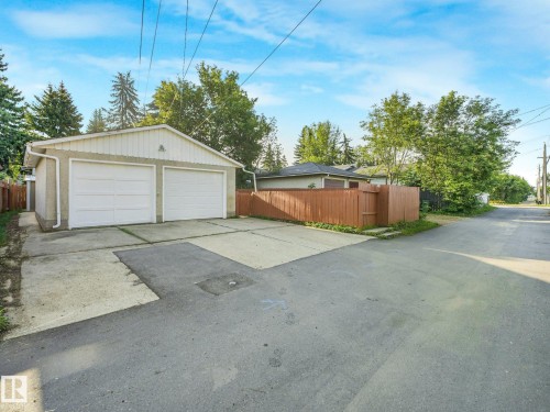 Detached two-car garage with two white panel garage doors, concrete driveway, and brown privacy fencing - 6112 105A Street Nw, Edmonton, AB - Outdoor