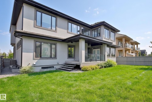 Stucco exterior with dark trim windows, covered outdoor patio space, glass panel railings, and a manicured lawn area - 3644 Westcliff Way Sw, Edmonton, AB - Outdoor With Deck Patio Veranda