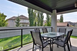 Covered patio with a concrete surface, supported by a substantial column, and enclosed by a glass railing with a dark frame - 