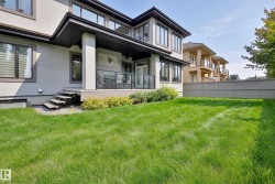 Expansive green lawn with a covered patio, glass railing, and exterior steps - 