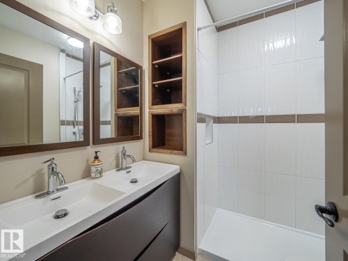 Dual vanity with integrated sinks, framed mirrors, built-in wooden shelving, and a tiled shower with an integrated bench - 97 Astoria Point(E), Devon, AB - Indoor Photo Showing Bathroom