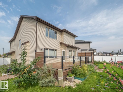 Rear elevation featuring horizontal siding, multi-level wood deck, glass panel railing, and a grass lawn with landscaping - 97 Astoria Point(E), Devon, AB - Outdoor