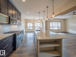 Kitchen featuring a gas range, hexagon tile backsplash, dark wood-finish cabinetry, and an island with a built-in sink - 