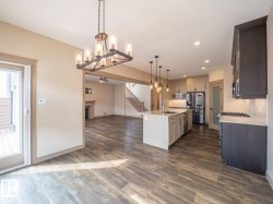 Expansive kitchen featuring a center island, pendant lighting, stainless steel appliances, and wood-finish flooring throughout - 