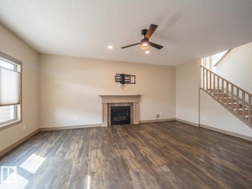 Wood-finish flooring throughout, featuring a fireplace with a mantel, a ceiling fan, and staircase with wood railing - 97 Astoria Point(E), Devon, AB - Indoor With Fireplace