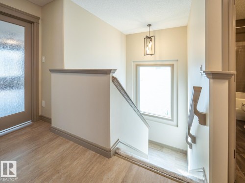 Wood-finish flooring, staircase with a window, modern pendant light fixture, and a door with frosted glass - 97 Astoria Point(E), Devon, AB - Indoor Photo Showing Other Room