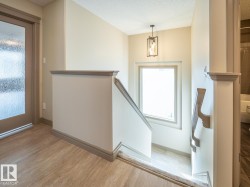 Wood-finish flooring, staircase with a window, modern pendant light fixture, and a door with frosted glass - 