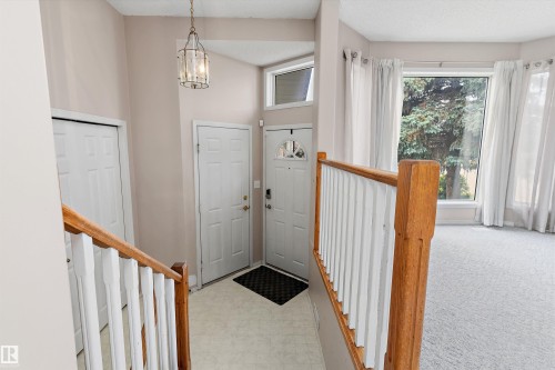 Entryway featuring a decorative pendant light, wood-finish handrail, and front door with transom window - 851 112A Street Nw, Edmonton, AB - Indoor Photo Showing Other Room
