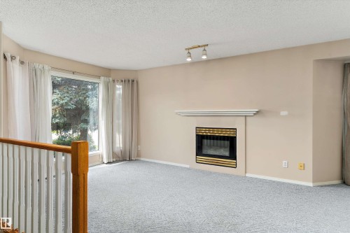 Living area featuring a fireplace with a mantel, track lighting, light-toned carpeting, and a large window - 851 112A Street Nw, Edmonton, AB - Indoor With Fireplace