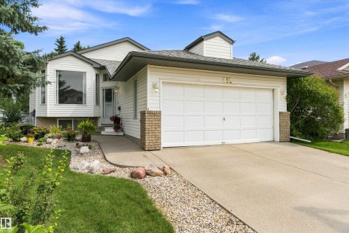 White siding exterior with a prominent bay window, attached garage, concrete driveway, and front landscaping featuring gravel and mature greenery - 851 112A Street Nw, Edmonton, AB - Outdoor