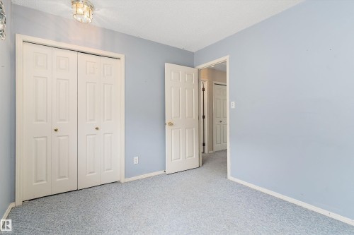 Textured wall-to-wall carpeting, light blue wall finishes, ceiling-mounted light fixture, white bi-fold closet doors, and white interior door - 851 112A Street Nw, Edmonton, AB - Indoor