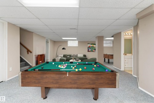 Finished lower level featuring a recreational space, a carpeted stairwell with wood railing, recessed lighting, and an adjacent bathroom with a vanity - 851 112A Street Nw, Edmonton, AB - Indoor Photo Showing Other Room