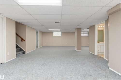 Expansive carpeted floor area with recessed lighting, light-toned walls, and a visible staircase with a wooden handrail - 851 112A Street Nw, Edmonton, AB - Indoor Photo Showing Basement