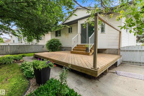 Expansive wood deck with stairs, white siding exterior, sliding glass door, and mature landscaping - 851 112A Street Nw, Edmonton, AB - Outdoor