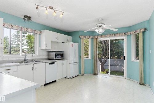 White cabinetry, stainless steel sink, track lighting, ceiling fan, and sliding glass door - 851 112A Street Nw, Edmonton, AB - Indoor Photo Showing Kitchen With Double Sink