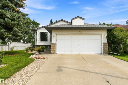 White siding exterior with brick accents, prominent two-car garage, front yard with mature landscaping, bay window, and concrete driveway - 851 112A Street Nw, Edmonton, AB - Outdoor