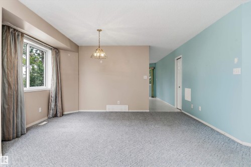 Spacious living area featuring neutral wall finishes, carpet flooring, large windows with natural light, and a pendant light fixture overhead - 851 112A Street Nw, Edmonton, AB - Indoor Photo Showing Other Room