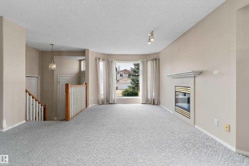 Neutral tone wall paint, patterned carpet flooring, built-in fireplace with mantel, bay window, and a staircase with wood railing - 851 112A Street Nw, Edmonton, AB - Indoor