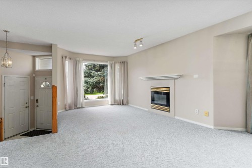 Inviting living space featuring a bay window, a built-in fireplace with a mantel, and light-toned carpeting - 851 112A Street Nw, Edmonton, AB - Indoor With Fireplace