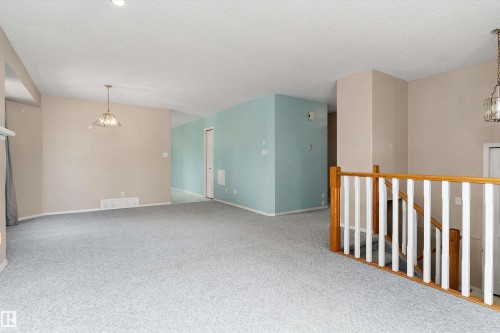 Carpeted living space with a suspended light fixture, painted walls, and a wooden handrail with white spindles - 851 112A Street Nw, Edmonton, AB - Indoor Photo Showing Other Room