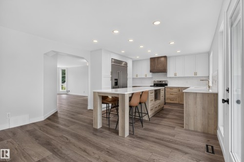 Contemporary kitchen with wood-finish flooring, white cabinetry, a large center island, built-in stainless steel refrigerator, and a dark wood range hood - 229 Hillcrest Crest, Sherwood Park, AB - Indoor